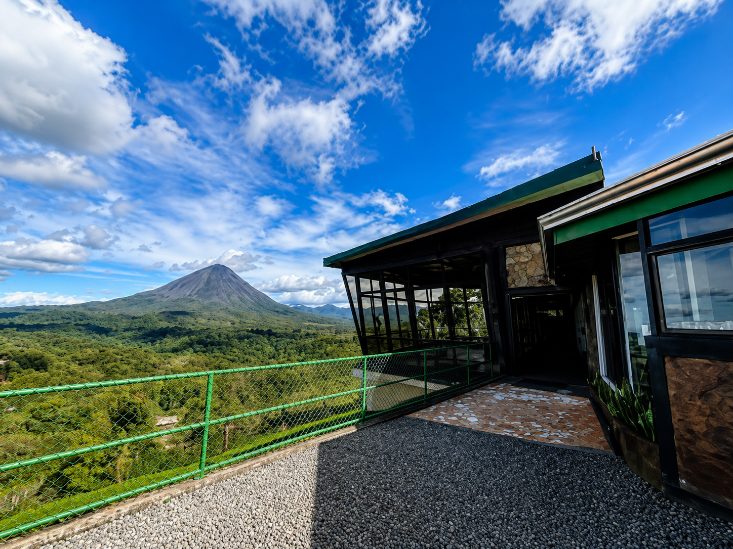 La Roca Bistró exterior terrace overlooking the rainforest with Arenal Volcano rising beside the building.