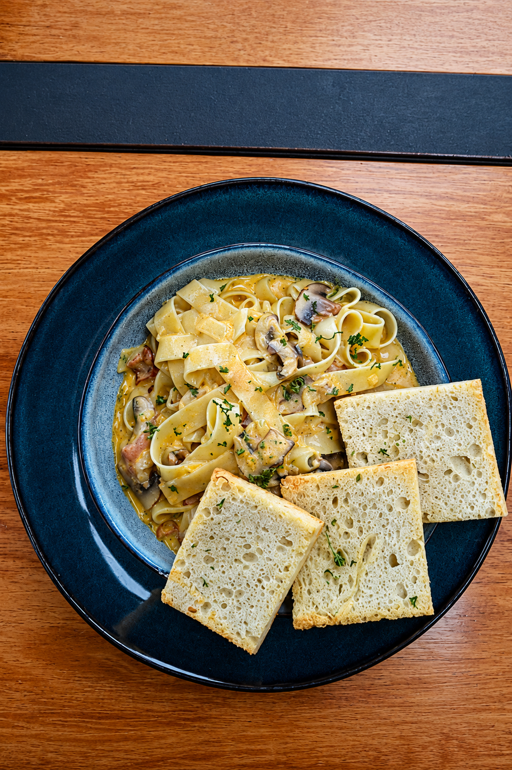 Creamy pasta dish with mushrooms and toasted bread served on a deep blue plate.