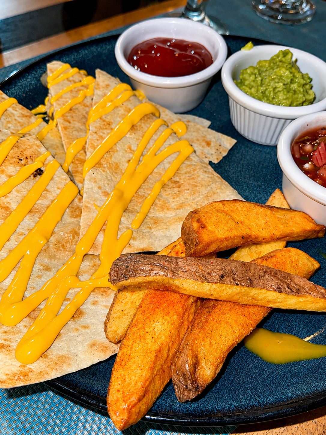 Quesadilla platter with guacamole, salsa, and potato wedges on a blue plate.
